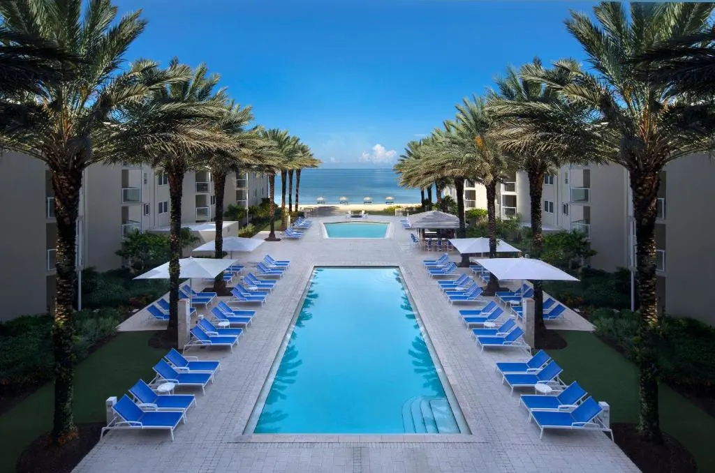 Trees and chairs line the outdoor pool with a view of the ocean at Edgewater Beach Resort in Naples, Florida