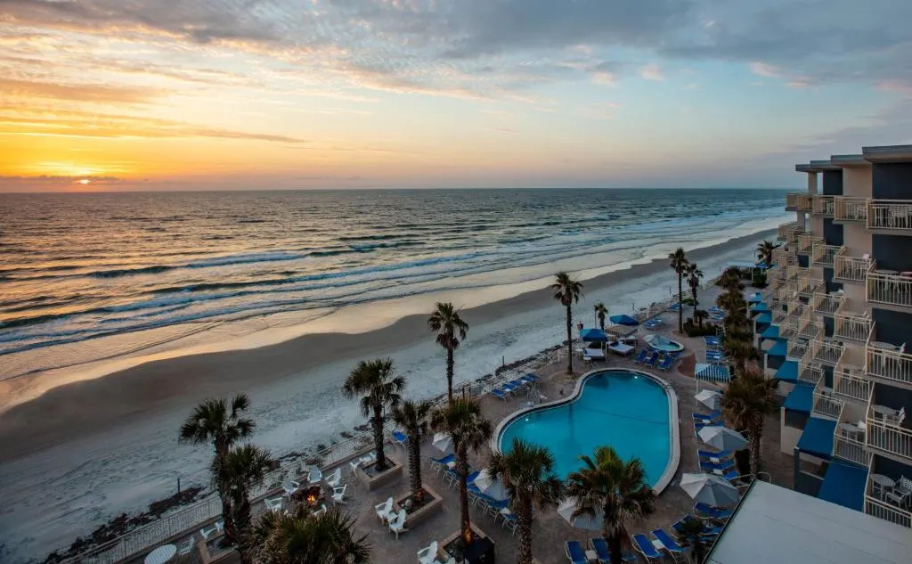 View of the outdoor pool, beach, and ocean at sunset from The Shores Resort and Spa Daytona Beach